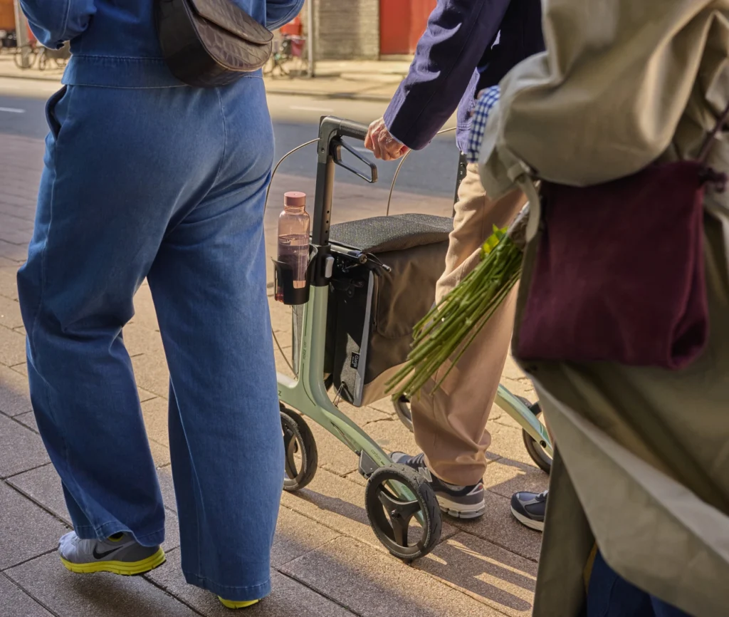 Walking with a Rollz Air wheeled rollator through a city. The walker is equipped with a cup holder and double luxury bags